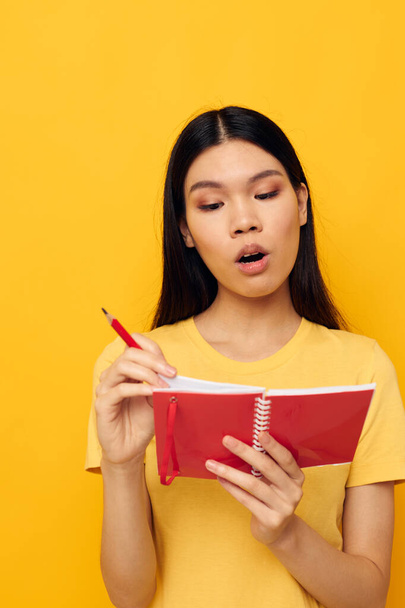 Charming young Asian woman in a yellow t-shirt red notebook training studio model unaltered - Foto, afbeelding