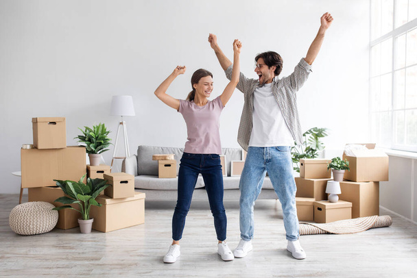 Satisfecho europeo millennial chico y mujer se divierten bailando en el interior de la habitación entre cajas, celebrando el alquiler de casa - Foto, Imagen