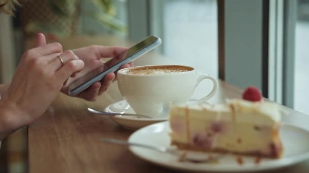 A nő a kávézóban reggelizik, okostelefont használ a kávézóban - Felvétel, videó