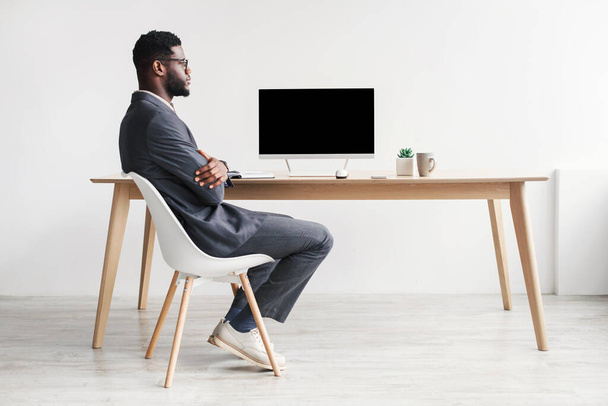 Full length of young black entrepreneur in office wear using computer with mockup for website design against white wall - Photo, Image