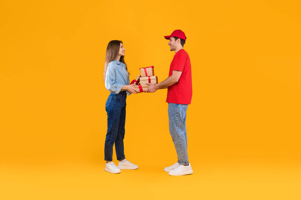 Kurier übergibt Geschenkboxen an Kundin vor gelbem Hintergrund - Foto, Bild