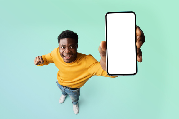 Возбужденный черный парень демонстрирует смартфон с чистым белым экраном, показывая свободное место для вашей рекламы, макет - Фото, изображение