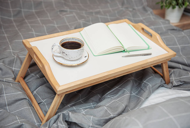 Breakfast in bed. Coffee and notebook on a wooden tray. Work at home concept. - Foto, imagen