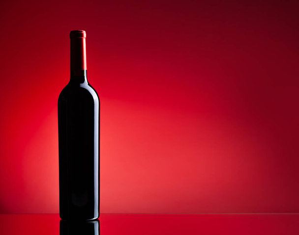 Κόκκινο κρασί μπουκάλι πάνω από το κόκκινο φόντο με αντίγραφο χώρου - Φωτογραφία, εικόνα