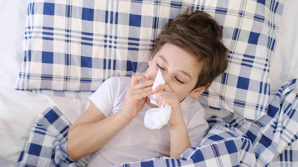Influenza fredda infantile tessuto che soffia naso che cola. Il bambino e 'sdraiato a letto e soffia il naso nella carta velina a casa. Allergia, influenza - Foto, immagini