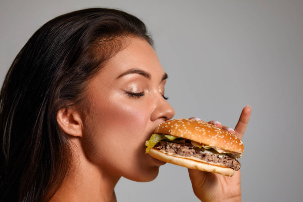 cheat meal concept. athlete woman is posing with fast food on light gray background, studio shot. young sporty woman is holding fast food close up. - 写真・画像