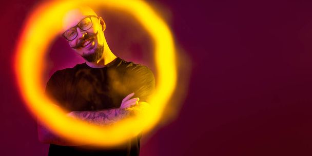 young bald man looking at the camera through a ring of smoke. color filters. Vaping concept  - Фото, изображение