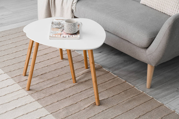 Table with cup, magazine and eyeglasses on new carpet in room - Фото, изображение