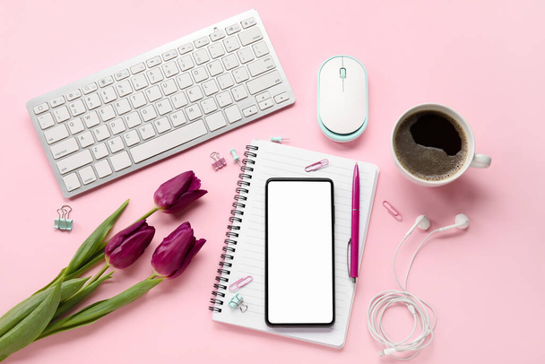 Cep telefonlu kompozisyon, bir fincan kahve, klavye ve pembe arka planda çiçekler - Fotoğraf, Görsel