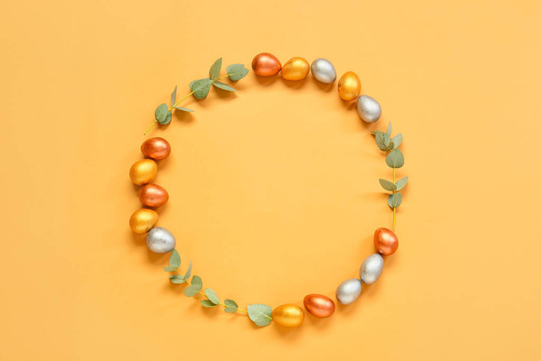 Frame made of Easter eggs and eucalyptus branches on orange background - Foto, imagen