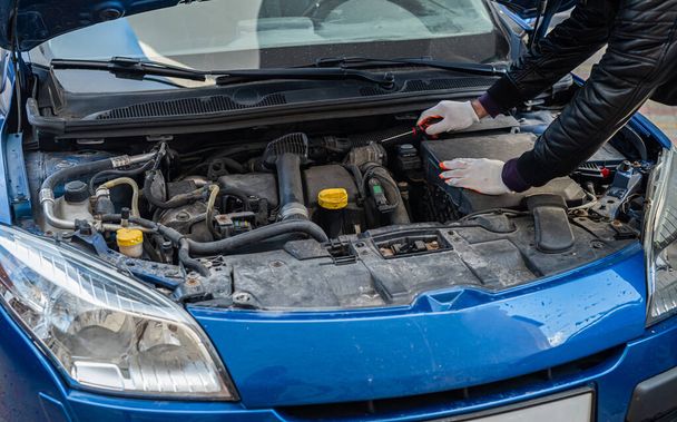 a man in gloves looks under the hood of an open car for a breakdown. Concept of owner and car breakdown - Photo, Image