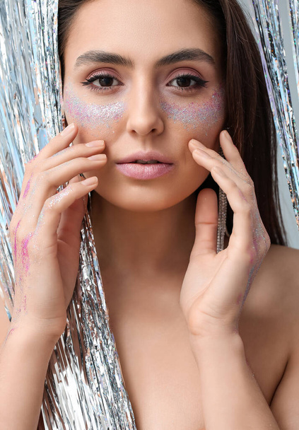Beautiful young woman with glitters on her face against light background - Fotoğraf, Görsel