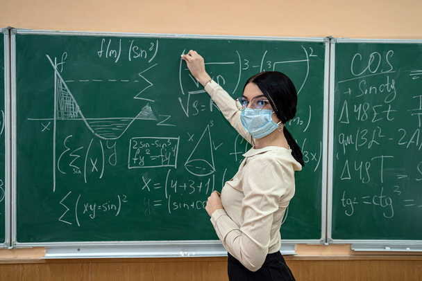 insegnante di sesso femminile con maschera imparare lezione di matematica a scuola durante la pandemia di coronavirus, infezione covid19. Distanziamento sociale - Foto, immagini