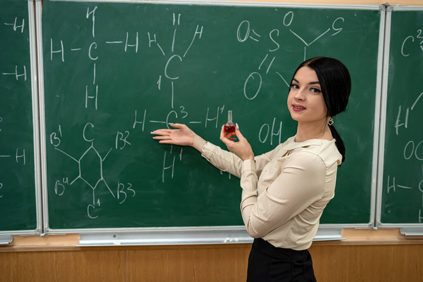 young pretty teacher learn lesson on chemistry and standing near blackboard with chemical formula, education concept - Photo, Image