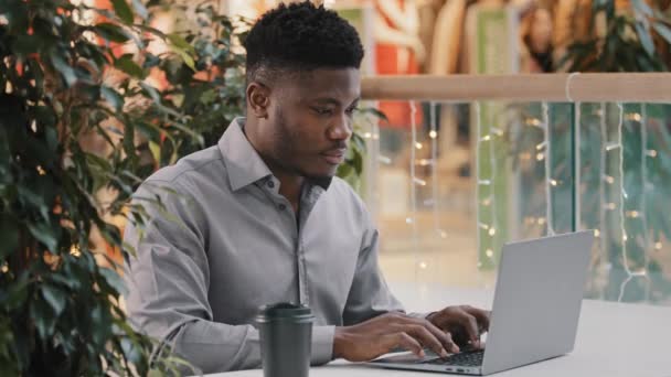 Επικεντρωμένος νεαρός αφροαμερικάνος ελεύθερος επαγγελματίας που κοιτάζει προσεκτικά την οθόνη lap-top που εργάζεται εξ αποστάσεως δακτυλογραφώντας το επαγγελματικό άρθρο γραφής ηλεκτρονικού ταχυδρομείου που κουβεντιάζει στο κοινωνικό δίκτυο on-line χρησιμοποιώντας την εφαρμογή υπολογιστών - Πλάνα, βίντεο