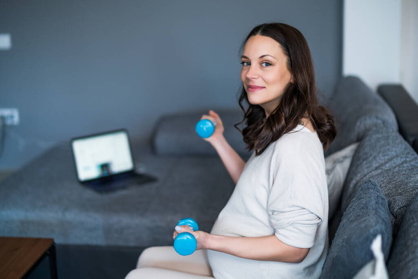 Portrait of pregnant happy woman who is exercising with weights at home.  - Foto, afbeelding