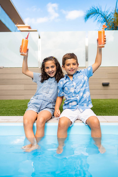 Twee kinderen drinken sinaasappelsap in het zwembad - Foto, afbeelding