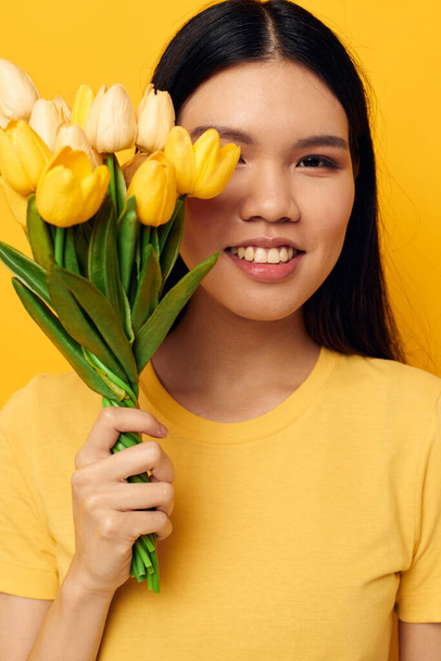 woman in a yellow t-shirt t-shirt with a bouquet of flowers holiday yellow background unaltered - Valokuva, kuva