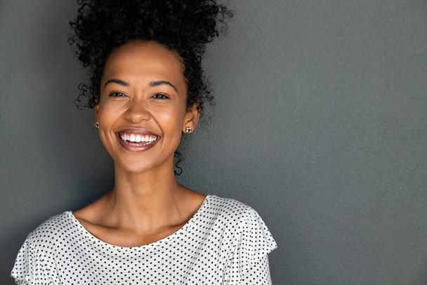 Portrait of cheerful young woman laughing against grey background. Happy african american girl with curly hair smiling against gray wall with copy space. Close up face of young black woman smiling. - Photo, Image