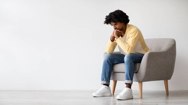 Pensées lourdes. Portrait de jeune homme afro-américain pensif assis dans un fauteuil - Photo, image