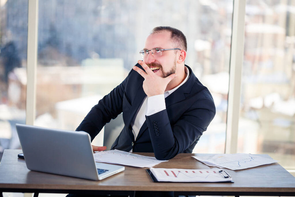 Korporacyjny szaleniec siedzi przy komputerze w biurze i wariuje, emocjonalny portret mężczyzny przy stole. Szalony pracownik w swoim miejscu pracy - Zdjęcie, obraz