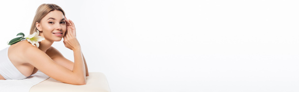 jovem feliz com flor de ombro nu deitado na mesa de massagem isolada no branco, banner - Foto, Imagem