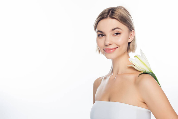 cheerful young woman with blooming flower on bare shoulder isolated on white  - Fotó, kép