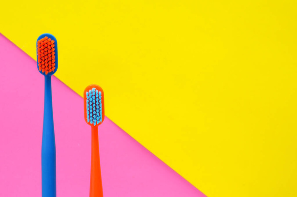две разноцветные зубные щетки на желто-розовом фоне. копировальное пространство - Фото, изображение
