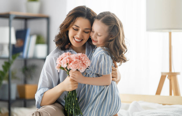 Happy day! Child daughter is congratulating mother and giving her flowers. Mum and girl smiling and hugging. Family holiday and togetherness. - Φωτογραφία, εικόνα