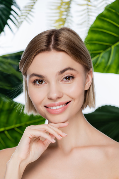 joyful young woman with perfect skin near green tropical leaves on white - Foto, immagini