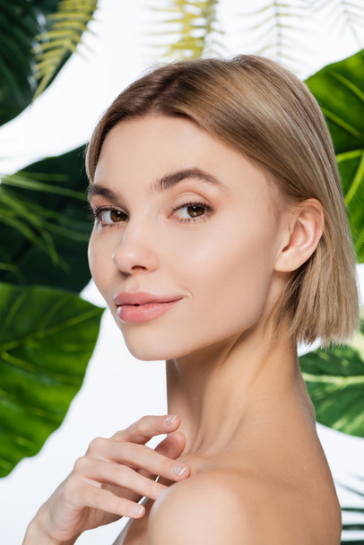 blonde woman with perfect skin looking at camera near palm leaves on white - Fotoğraf, Görsel