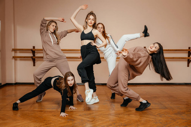 Ryhmä tyttöjä urheiluvaatteissa, esittävät talon tanssin elementtejä tanssistudiossa, tanssivat mielihyvin. Urheilunuorten käsite.  - Valokuva, kuva