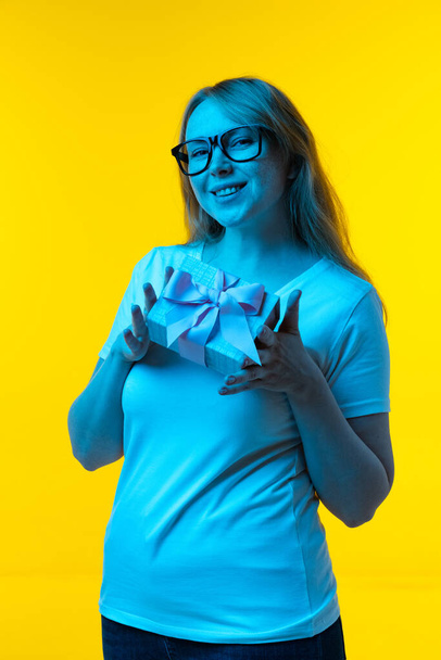 Beautiful young girl with freckles on her face isolated on yellow background in neon. Concept of wow emotions, facial expressions, ad, sales - Photo, Image
