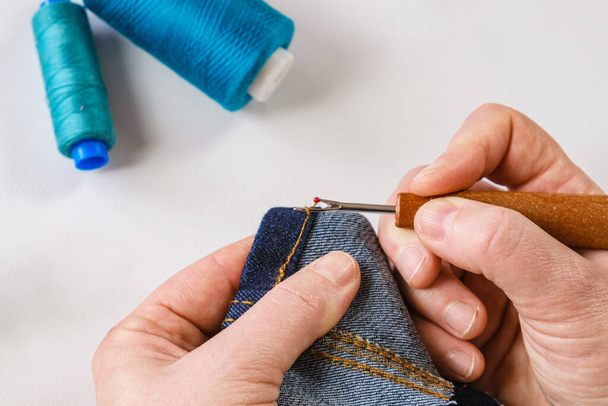 Woman seamstress rips a seam on a denim fabric with a seam ripper. Seamstress tools, mending clothes, altering jeans. - Photo, Image