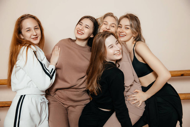 Retrato de cinco hermosas mujeres sonrientes en ropa deportiva, de pie juntas en aislamiento sobre un fondo gris, abrazándose, riendo.  - Foto, Imagen