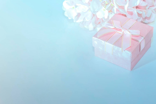 Festive background for a greeting card with a pink gift box with a bow and flowers of artificial hydrangea in pastel colors on a blue - Valokuva, kuva