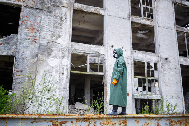 A dosimetrist scientist in protective clothing and a gas mask checks the level of radioactive radiation in the danger zone. Environmental pollution, disaster - Photo, Image