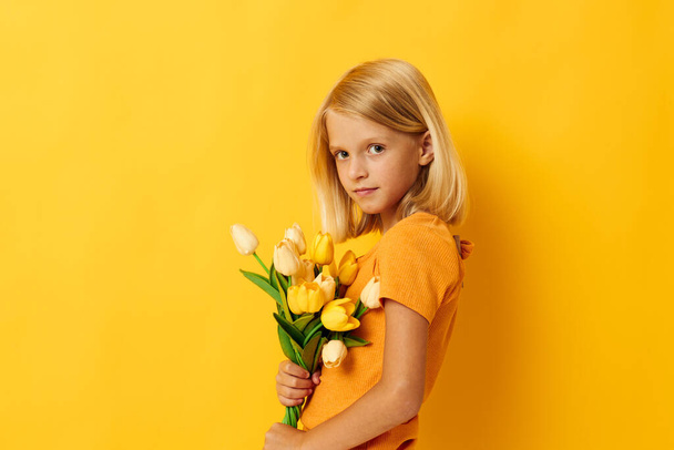 little girl with blond hair with a bouquet of yellow flowers on a yellow background - Zdjęcie, obraz