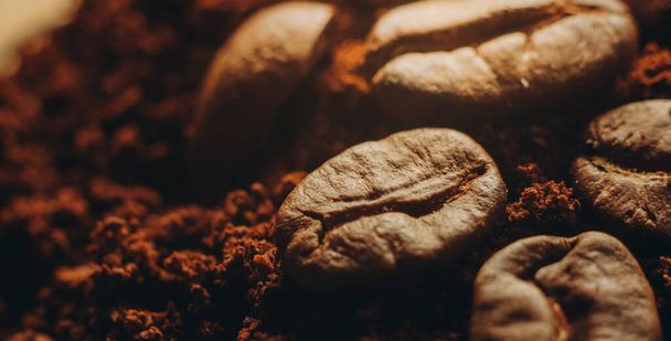 Roasted coffee beans lie in ground coffee. Aromatic roasted coffee close-up. - Photo, Image