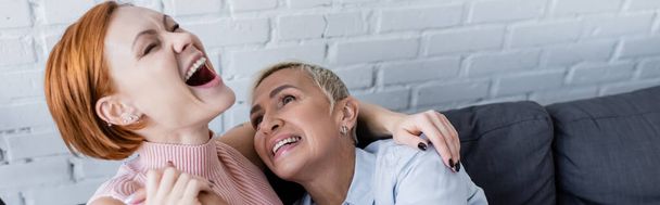 excited woman with closed eyes laughing near lesbian girlfriend at home, banner - Foto, Imagem