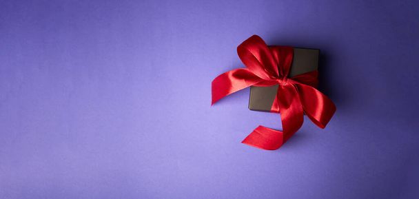 regalo nero con nastro rosso su sfondo viola. San Valentino. Concetto di compleanno o vacanze. Copia spazio - Foto, immagini