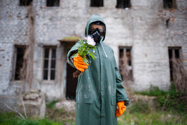 A dosimetrist scientist in protective clothing and a gas mask examines the danger zone. Close-up. flower in hands - Photo, Image