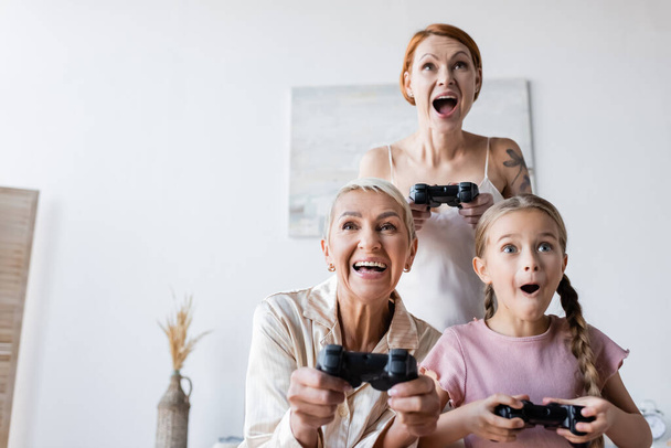 KYIV, UKRAINE - DECEMBER 8, 2021: Excited lesbian couple and child playing video game at home  - Fotó, kép