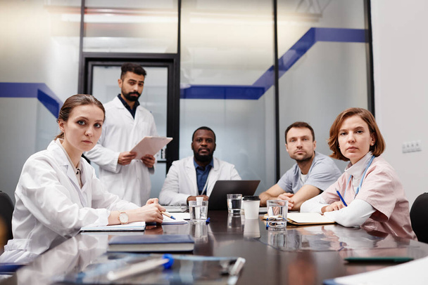 Група міжкультурних медичних експертів у лабораторних халатах, що сидять за столом
 - Фото, зображення