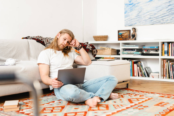Bearded blonde man working with laptop while sitting on floor at home - Foto, Bild