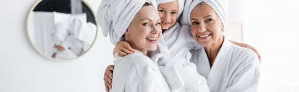 Pozytywne lesbijki w szlafrokach trzymające adoptowaną córkę w łazience, sztandar  - Zdjęcie, obraz