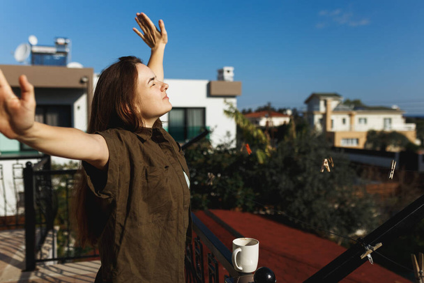 Retrato de uma mulher feliz mãos abertas bebendo café em uma varanda.Relaxe, pensando e olhando para longe. Ao ar livre em luz do sol desfrutando de seu chá da manhã. Na natureza de casa suave - Foto, Imagem