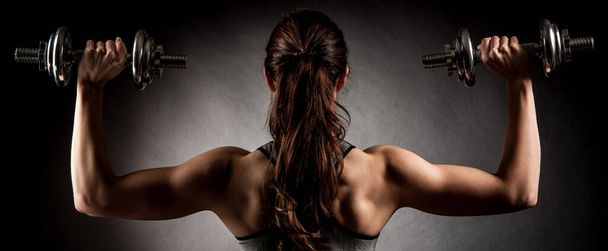 Atractive fit woman works out with dumbbells as a fitness conceptual over dark background. - Fotografie, Obrázek