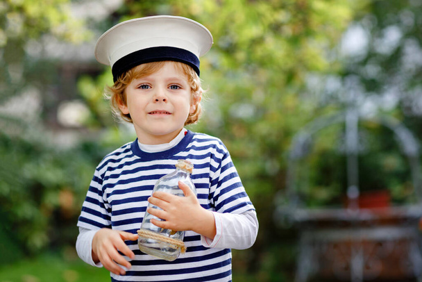 Szczęśliwy chłopczyk w czapce marynarza i mundurze bawiący się żaglowcem. Uśmiechnięte dziecko w przedszkolu marzące i bawiące się. Edukacja, zawód, koncepcja marzeń - Zdjęcie, obraz