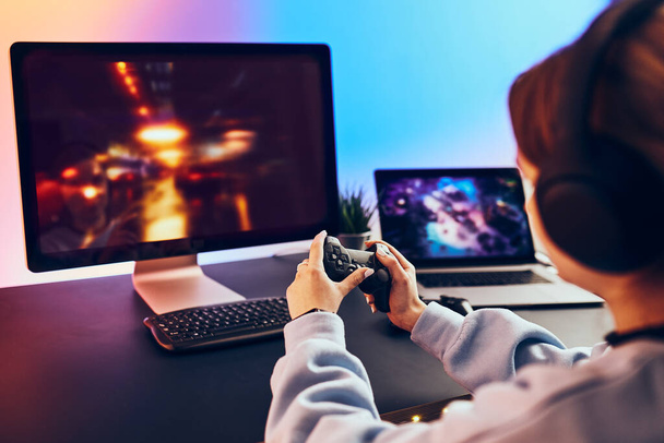 Teenager girl playing video game at home. Gamer holding gamepads sitting at front of screen. Streamer playing online in dark room lit by neon lights. Competition and having fun - Photo, Image